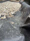 A close-up of a black geotextile fabric filter layer with small gray and white stones on the left side.