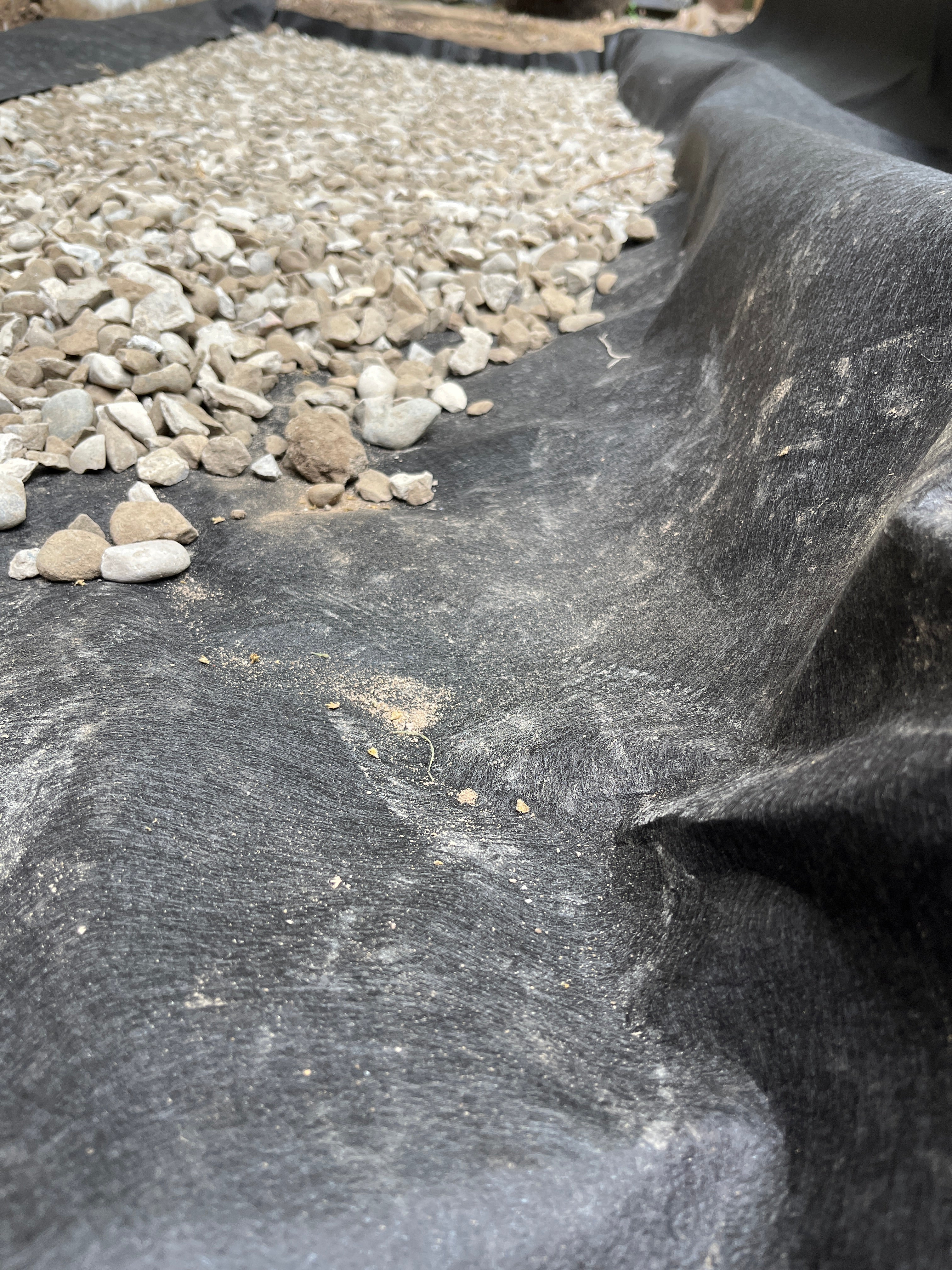 A close-up of a black geotextile fabric filter layer with small gray and white stones on the left side.