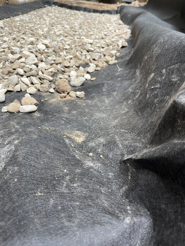 A close-up of a black geotextile fabric filter layer with small gray and white stones on the left side.